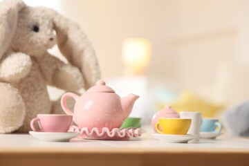 Tea set and stuffed bunny on white table indoors, closeup with space for text. Child's toy