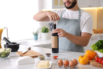 Man opening bottle of wine while cooking at table in kitchen, closeup
