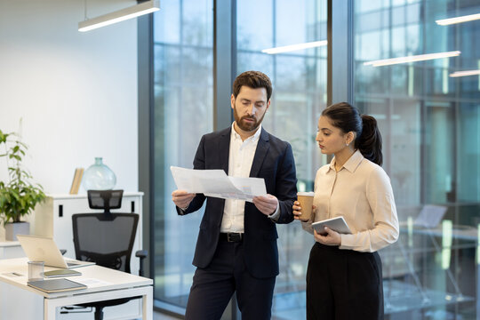 Two diverse business people are discussing important documents and financial data, collaborating on a project in a bright contemporary office environment