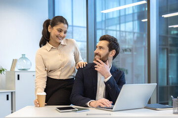 Happy business couple working together in a corporate office, sharing a moment of lighthearted connection with smiles, demonstrating positive work dynamics