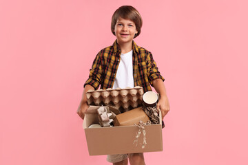 Recycling. Cute little boy with cardboard box full of different waste paper on pink background © New Africa