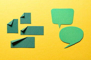 Green speech bubbles and paper memo notes with folded dog-ear earmark and copy space for text on yellow background, communication dialog concept top view flat lay