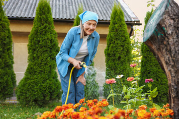 Senior woman watering beautiful flowers with hose in garden