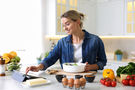 Smiling woman looking at recipe on tablet while cooking at table in kitchen - Powered by Adobe