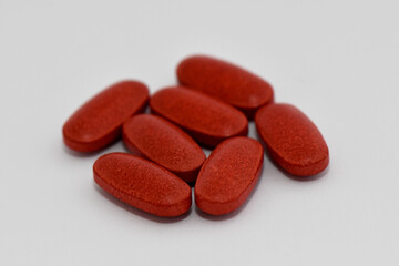 A small pile of red, oval-shaped pills or tablets are scattered on a white background, creating a clean and simple image for pharmaceutical or medical themes.