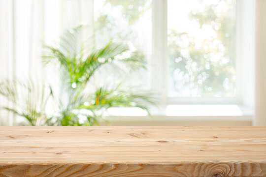 Empty wood table top on blurred curtained window and abstract greenery from garden background