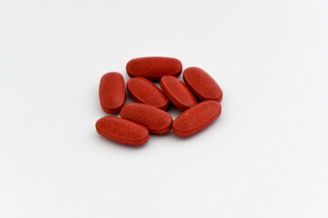 A small pile of red, oval-shaped pills or tablets are scattered on a white background, creating a clean and simple image for pharmaceutical or medical themes.