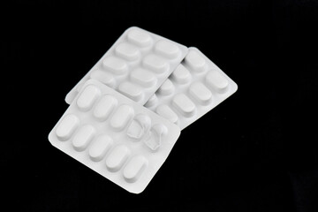 Two sealed blister packs and one partially opened blister pack with white pills on a black background, representing medicine, health, and wellness.