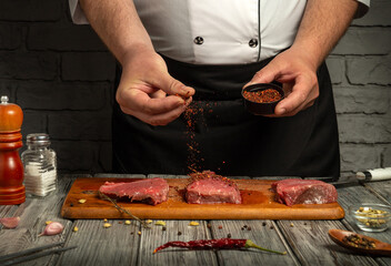 A chef in a black apron sprinkles spices over fresh cuts of steak on a wooden board. The kitchen has a warm, rustic ambiance, perfect for cooking