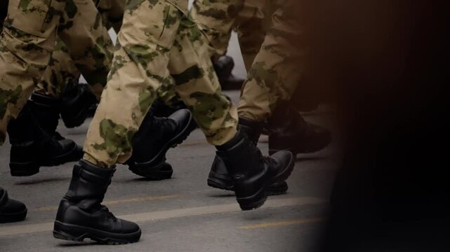 Close-up view of soldiers in camouflage uniforms marching in formation on a city street, black combat boots stepping in unison during a disciplined military parade or drill sequence