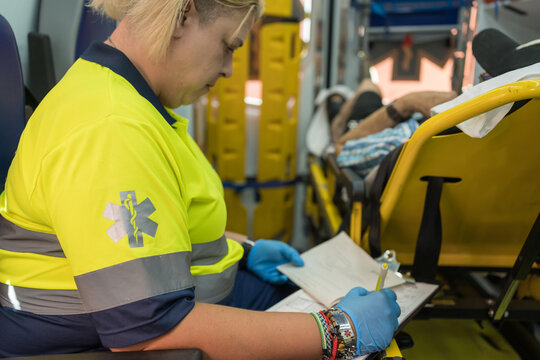 Female paramedic taking notes inside ambulance with patient in background