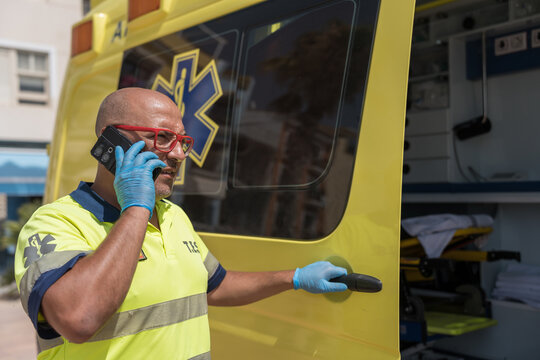 Paramedic wearing protective gloves talking on phone near ambulance