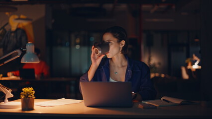 Late worker developing project overtime drinking coffee at dark office closeup. 