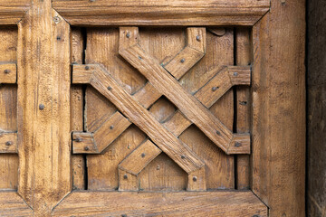 Weathered wooden door panel with decorative crossed planks, close up photo