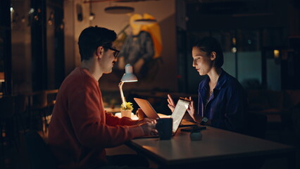 Two late managers talking at dark workspace looking laptops office closeup.