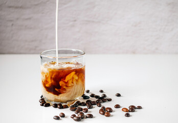 Latte coffee, Milk pouring from a milk jug into a glass of iced coffee with coffee beans on a white background