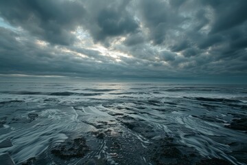 Fototapeta premium Ocean waves crashing on a rocky beach under a dramatic cloudy sky, creating a moody and atmospheric scene