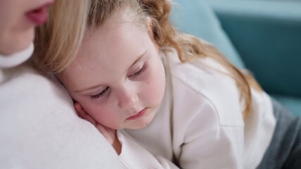 Little girl with closed eyes resting head on mother chest while cuddling together on couch, peaceful family moment showing love, comfort, warmth, trust, tenderness, maternal bond, childhood relaxation