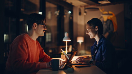 Smiling colleagues working overtime in dark office coworking space closeup. 