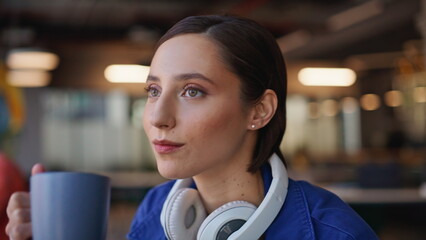 Dreamy girl sipping tea sitting cozy cafeteria with headphones on neck closeup. 