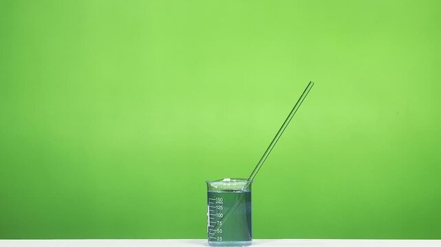 Glass rod placed inside beaker with blue liquid on green background laboratory scene