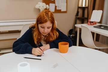 A teenage girl studies in the living room during evening hours, drinking coffee while focusing on...