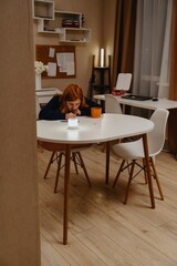 A teenage girl studies in the living room during evening hours, drinking coffee while focusing on homework. Captures authentic student life and modern study routines