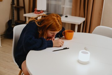 A teenage girl studies in the living room during evening hours, drinking coffee while focusing on...