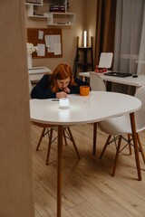 A teenage girl studies in the living room during evening hours, drinking coffee while focusing on homework. Captures authentic student life and modern study routines