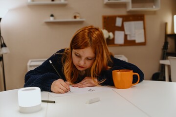 A teenage girl studies in the living room during evening hours, drinking coffee while focusing on...