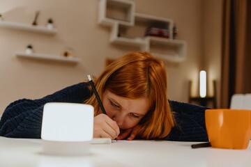 A teenage girl studies in the living room during evening hours, drinking coffee while focusing on...