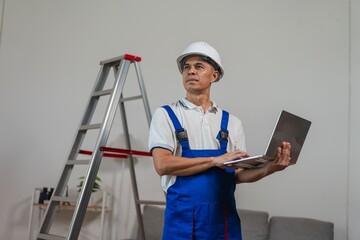 Young construction worker with laptop standing beside ladder in modern interior space, planning project for renovation or repair work © WITTAYA  ANGMUJCHA