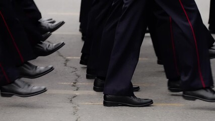 Close-up view of uniformed personnel marching in synchronized formation, polished black shoes and navy trousers stepping in cadence along a roadway during a disciplined drill