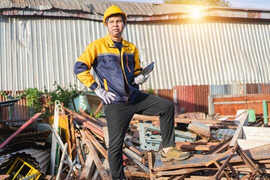 Confident Construction Worker Posing on Pile of Scrap Metal in Industrial Setting