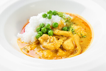 Bowl of white rice with green peas and creamy yellow curry featuring meat and vegetables. Vibrant colors, top view, appetizing presentation, Asian-inspired dish.