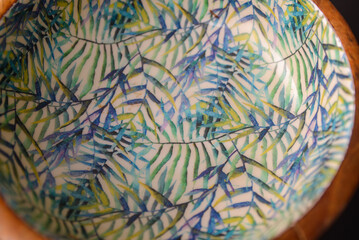 A round wooden bowl with hand-painted leaves on the inside that looks a bit like a jungle
