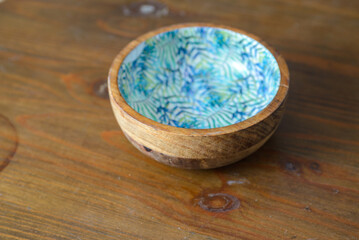 A round wooden bowl with hand-painted leaves on the inside that looks a bit like a jungle