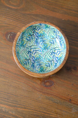 A round wooden bowl with hand-painted leaves on the inside that looks a bit like a jungle