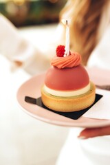 Young woman celebrating birthday holding cake with lit candle in warm light