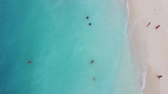 Stunning aerial footage captured directly from above, showing people sunbathing and swimming along a tropical beach. The water is an unreal turquoise, beach Kendwa
