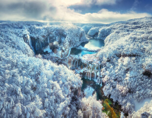Aerial drone view of frozen waterfalls and turquoise lakes in snowy forest at sunrise. Plitvice Lakes National Park, Croatia. Winter landscape with icy cascades, trees in snow. Scenic nature. Top view