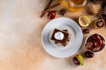 Homemade autumn taste chestnut pie bars. Freshly baked chestnut bars with whipped cream on it, with autumn decor and spices on beige table background, copy space 