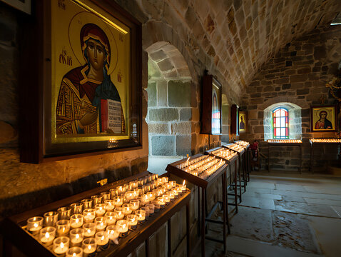 Rows of glowing votive candles illuminate a dimly lit stone church interior with a religious icon on the left wall All Saints’ Day