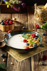 A delightful fresh granola bowl topped with vibrant berries and creamy yogurt is beautifully arranged on a rustic wooden table, surrounded by an array of colorful fruits
