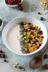 Breakfast bowl filled with yogurt, granola, and fresh berries enjoyed on a light stone surface during morning hours