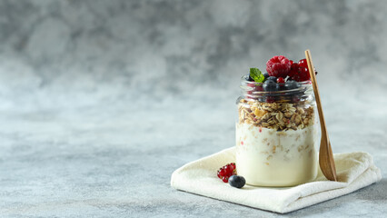 Delicious yogurt parfait with granola and berries served in a glass jar on a soft cloth against a neutral background