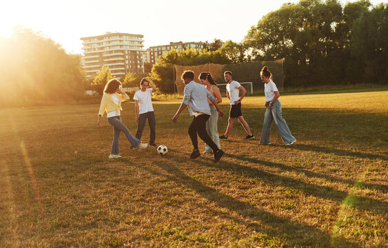 Fototapeta Males and females. Young friends are having fun on the field with soccer ball