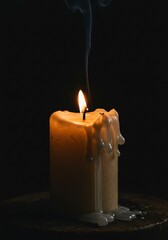 Solitary candle flame illuminates the darkness with dripping wax and smoke