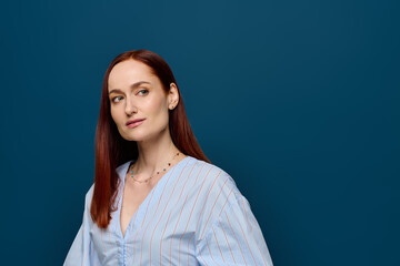 A beautiful woman with striking red hair poses elegantly in a light blue blouse