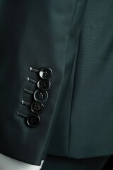 Close-up of a dark-green suit sleeve showcasing a row of black buttons and subtle sheen of the fabric.  The image highlights the tailoring details